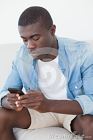 Casual man sitting on sofa texting on phone