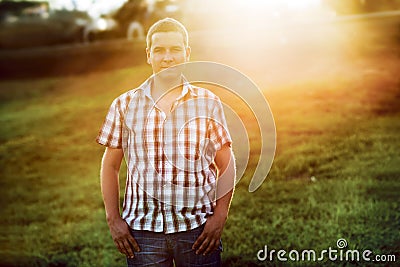 Casual man standing on the green grass in the park on the sunset