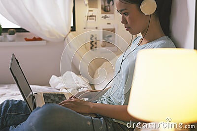 Casual young woman sitting on bed and using laptop at home.