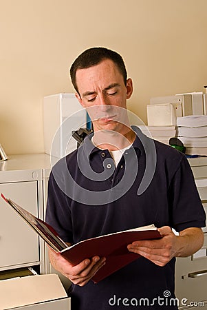 Caucasian male in file room reading papers inside a folder