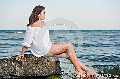 Caucasian teen girl in bikini and white shirt lounging on lava rocks by the ocean