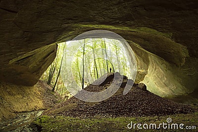 Cave entrance in huge cliff in the forest with man standing in front