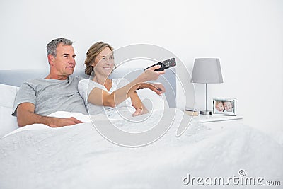 Cheerful couple watching tv in bed