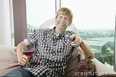 Cheerful mid-adult man with wine glass watching television on sofa at home