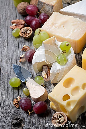 Cheeses, grapes and walnuts on a wooden background, top view