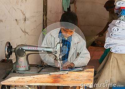 Child labor, boy sewing in booth on the market.