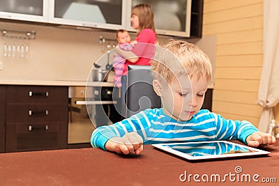 Child looking at touch pad while mother is cooking at home