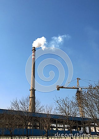 Chimney discharging white smoke into blue sky