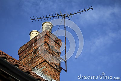 Chimney on a roof with TV aerial and blue sky with light cloud