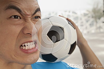 Close up of angry young man holding a soccer ball on his shoulder
