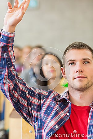 Close up of a male student raising hand by others in classroom