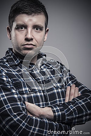 Close up portrait of young composed man wearing checked shirt with arms crossed