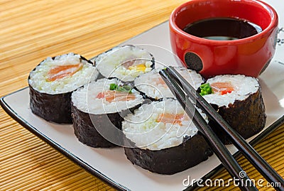 Close-up of six sushi rolls with soy sauce and chopsticks