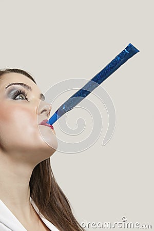 Close-up of a young woman blowing blue party blower against gray background