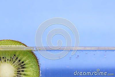 Closeup of a kiwi slice floating in sparkling water against an aqua blue background