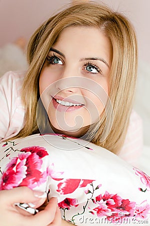 Closeup portrait of blue eyes beautiful happy smiling charming young blond woman lying on bed holding pillow and looking up