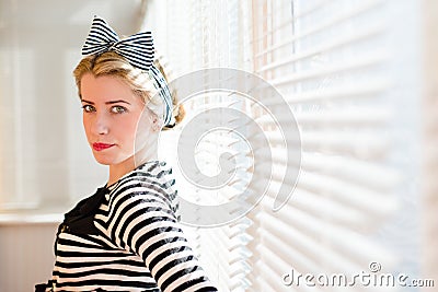 Closeup portrait of elegant pinup girl having fun posing & looking at camera on sun lighting blinds windows