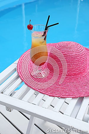 Cocktail with cherry on a beach table with a straw hat near