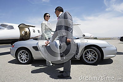 Colleague Holding Door Of Car For Colleague Near Private Aircraft