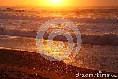 Waves rolling at beach by golden sunrise