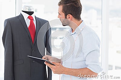 Concentrated fashion designer with digital tablet looking at suit on dummy