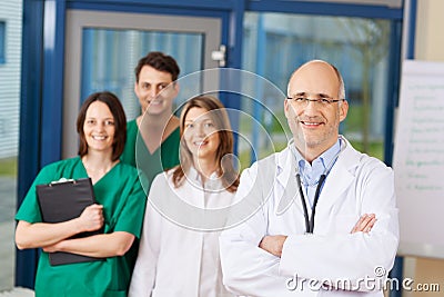 Confident Mature Male Doctor With Team In Background