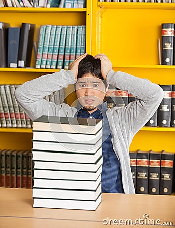 Confused Man Looking At Stacked Books In Library