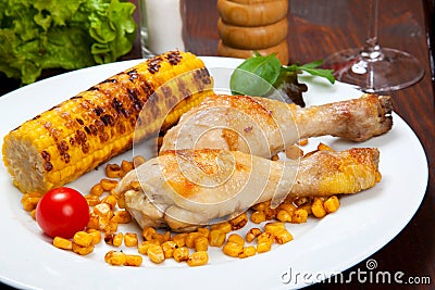 Cooked chicken thigh with a boundary of corn cob and salad