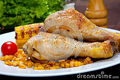 Cooked chicken thigh with a boundary of corn cob and salad