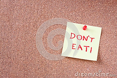 Cork board with pinned yellow note and the phrase dont eat written on it. room for text.