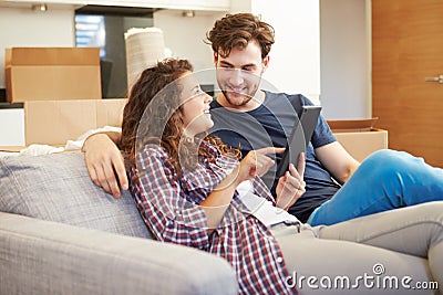 Couple Relaxing On Sofa With Digital Tablet In New Home