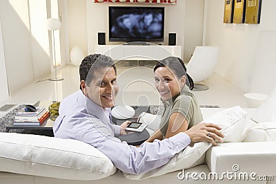 Couple With Remote Control Sitting On Sofa