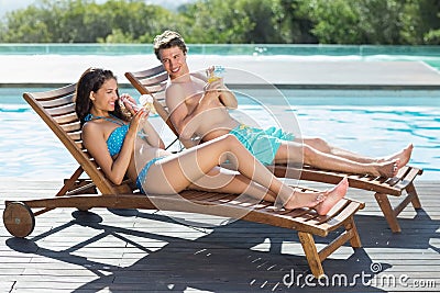 Couple sitting on sun loungers by swimming pool