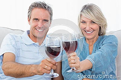 Couple toasting to the camera with red wine on the sofa