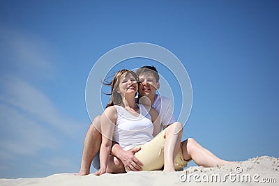 Couple in white shirts sitting on sand