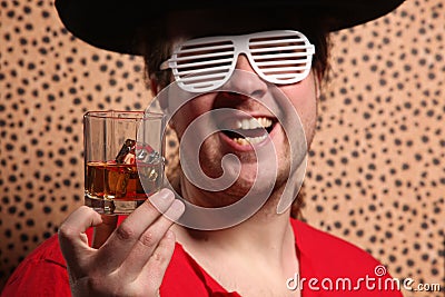 Crazy rock and rollerer with a big black hat, party glasses and a glass of whiskey in front of a cheetah skin background