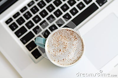A cup of coffee with milk foam on a laptop