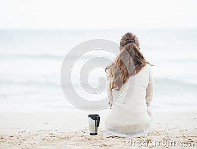 Cup of hot beverage near woman in sweater sitting on lonely beach