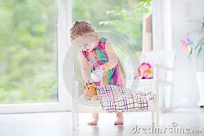 Curly toddler girl feeding her toy bear in white crib pla