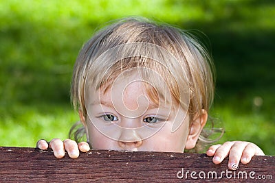 A curuos little boy hiding behind a bench