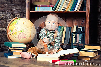 Cute baby boy sitting with globe, books and drawing pencils
