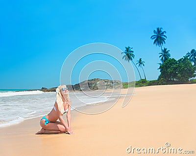 Cute blonde woman at ocean beach with waves against rock and palm