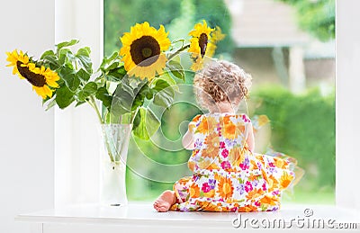 Cute curly baby girl next to sunflower bouquet