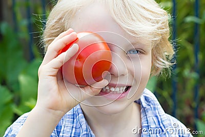 Cute healthy child holding an organic tomato over his eye