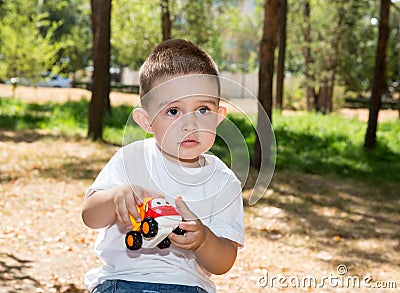 Cute little child boy plays with toy car in park on nature at summer.