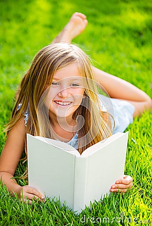 Cute little girl reading book outside on grass