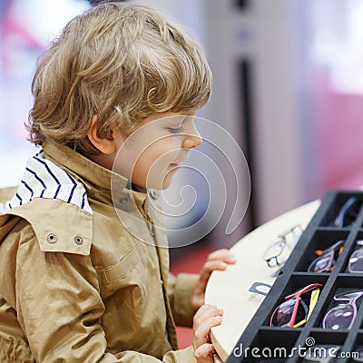 Cute little kid boy at optician store during choosing his new gl