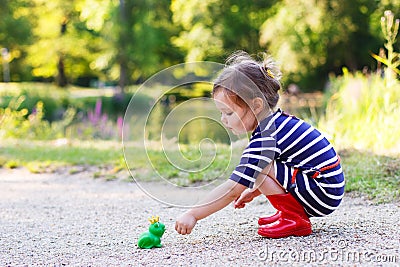 Cute princess girl in red rain boots playing with rubber toy fro