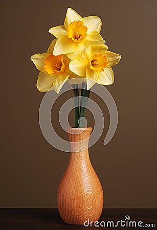  of three daffodils in a simple wooden vase with a brown background