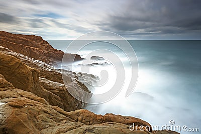 Dark red rocks, foam and waves, sea under bad weather.